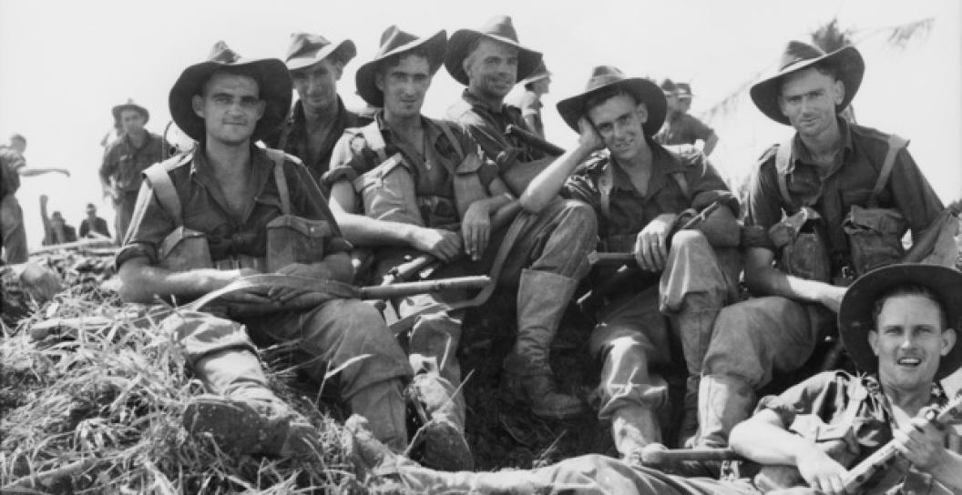 Seven smiling soldiers pose for photo while sitting on rough ground