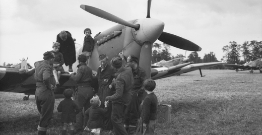Black and white photo of a Spitfire aircraft, with a pilot and children congregated around it.