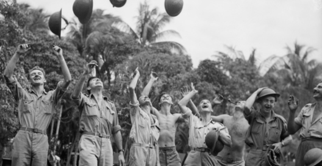 Black and white photo of soldiers throwing their helmets in the air in celebration
