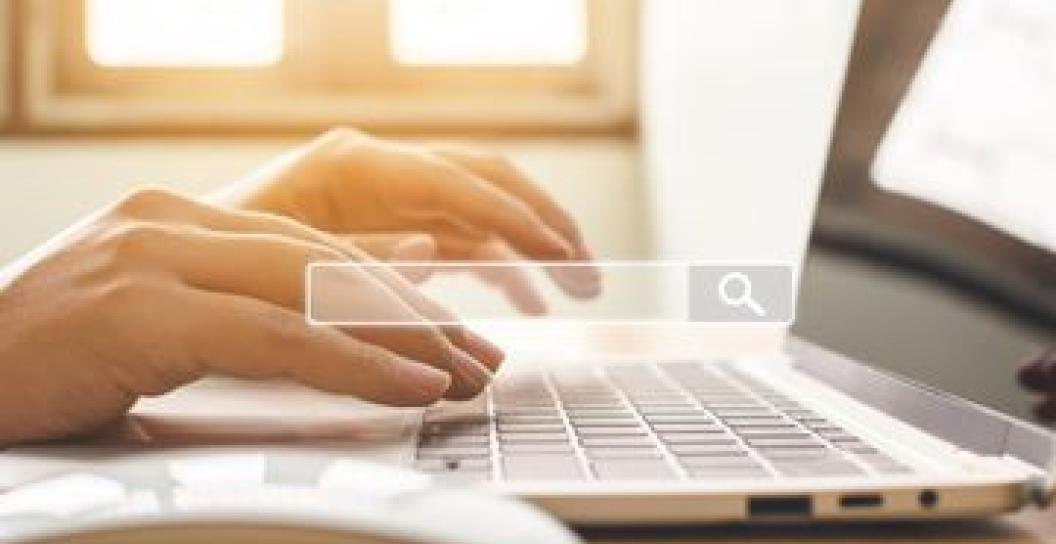 a hand on a keyboard and a mouse in the foreground, with a soft focus search toolbar overtop