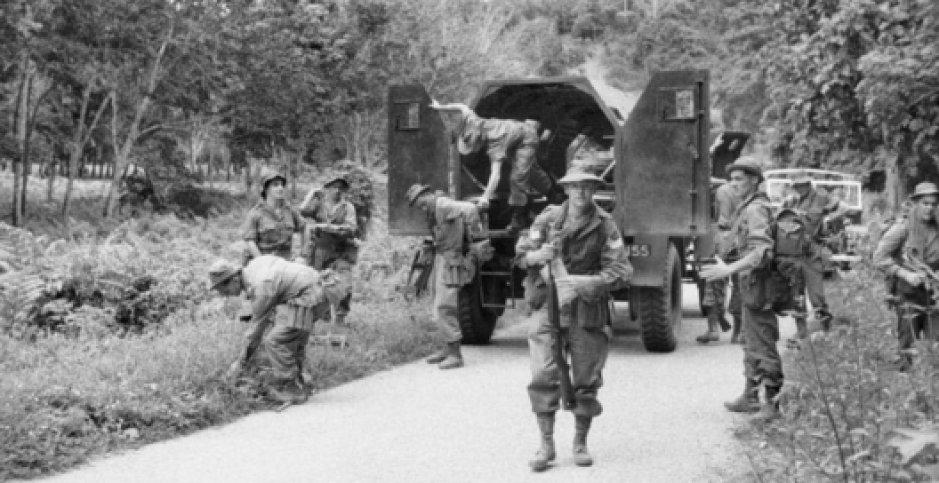 An Australian soldier waiting for his men to alight from an armoured truck on a road through a rubber estate in Perak, 1956.