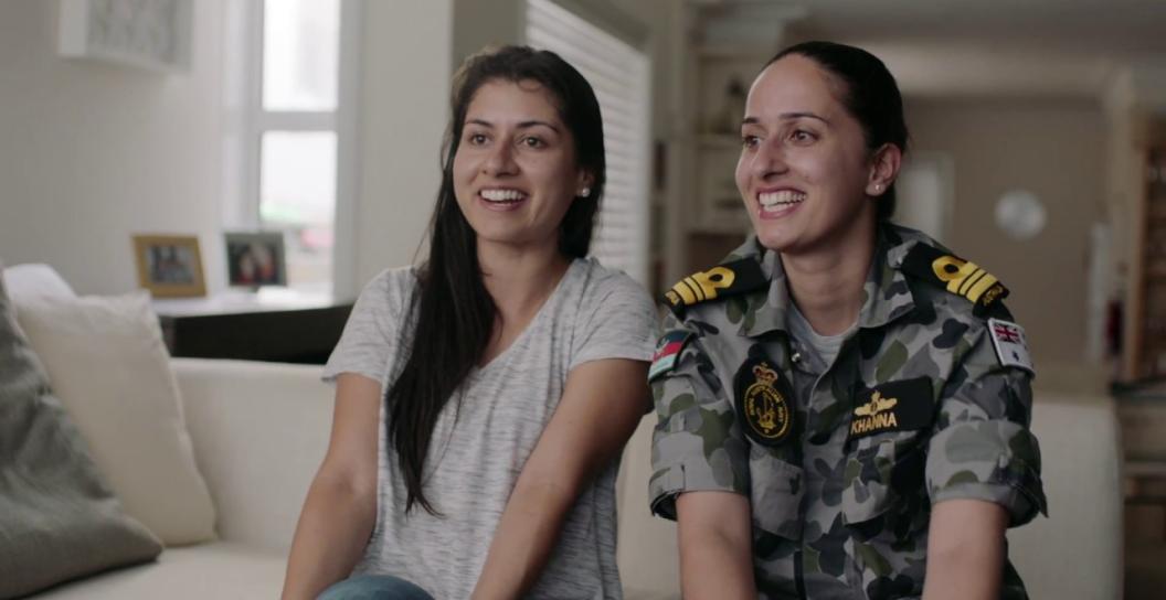 2 people sit on a couch, both from a multicultural background, one is wearing an adf uniform