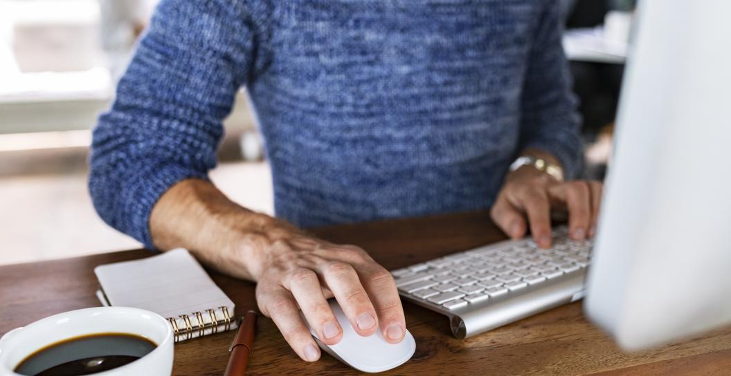 Person using home computer with a coffee next to them