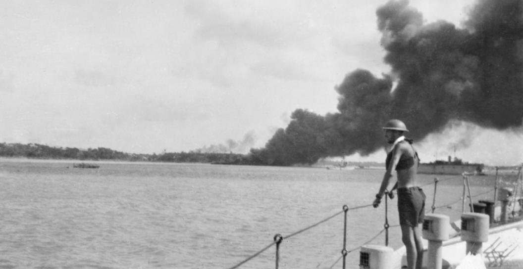 An unidentified sailor on board HMAS Platypus watches smoke billowing from MV Neptuna after she was destroyed during the first Japanese air raid on Darwin