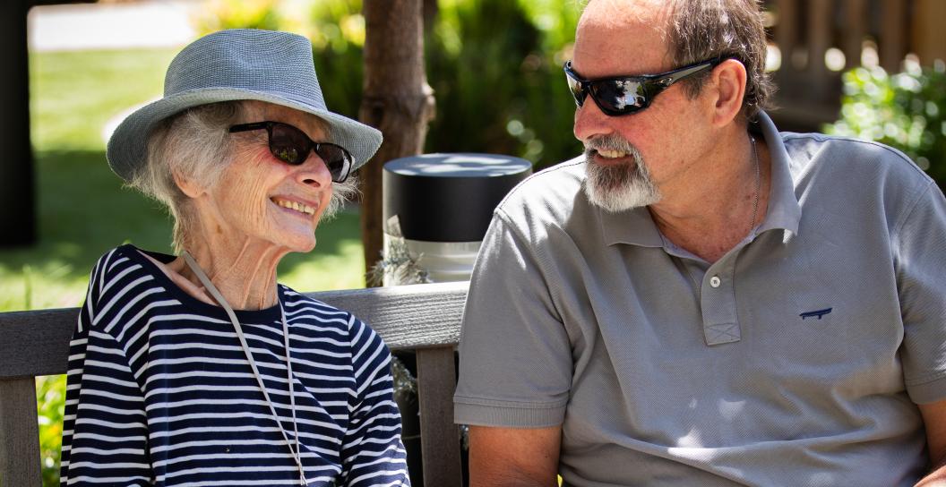 Old lady on bench smiling. Man is seated next to her.