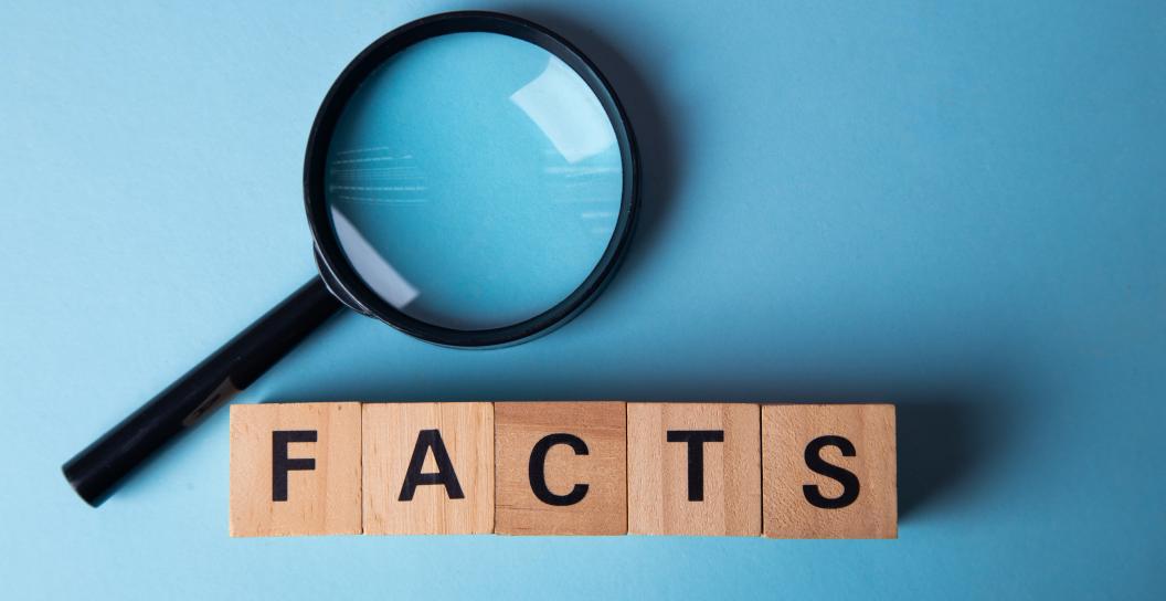 Wooden block letters spelling 'facts' rest on a clean blue surface, ready to be viewed with a magnifying glass.