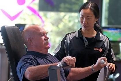 A young female exercise physiologist (EP) or physiotherapist assisting an elderly male patient in a gym.