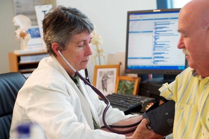 female doctor in her medical office checking male patients blood pressure 
