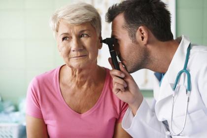An audiologist (hearing medical doctor) inspects an elderly woman's ear with an otoscope