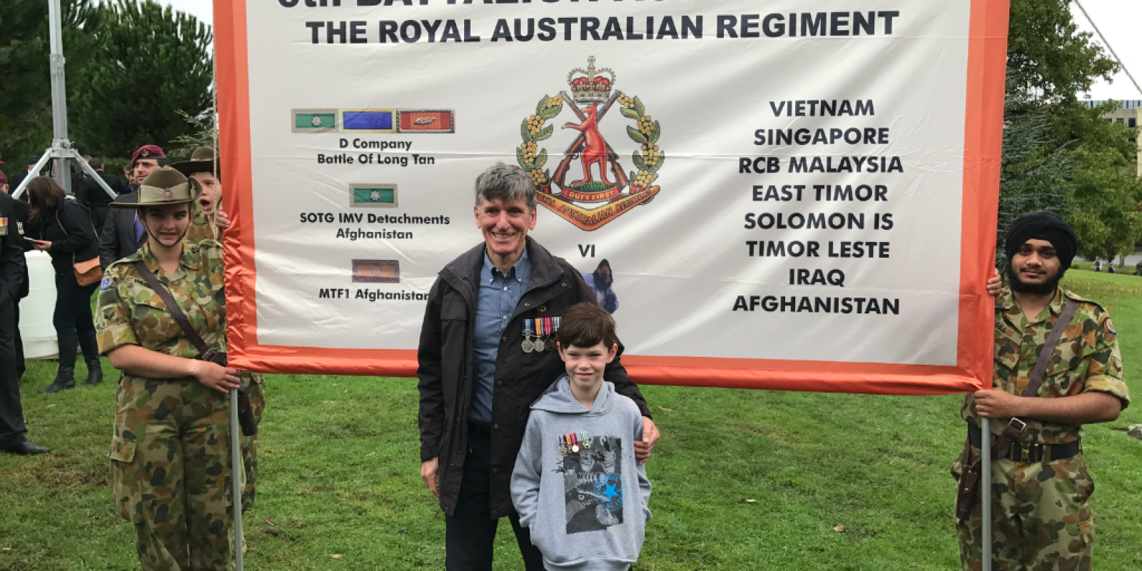 Peter standing in front of a 6th Battalion Association flag wearing his medals.