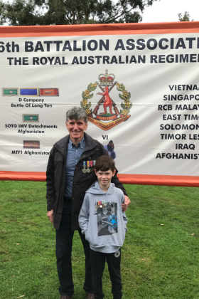 Peter standing in front of a 6th Battalion Association flag wearing his medals.